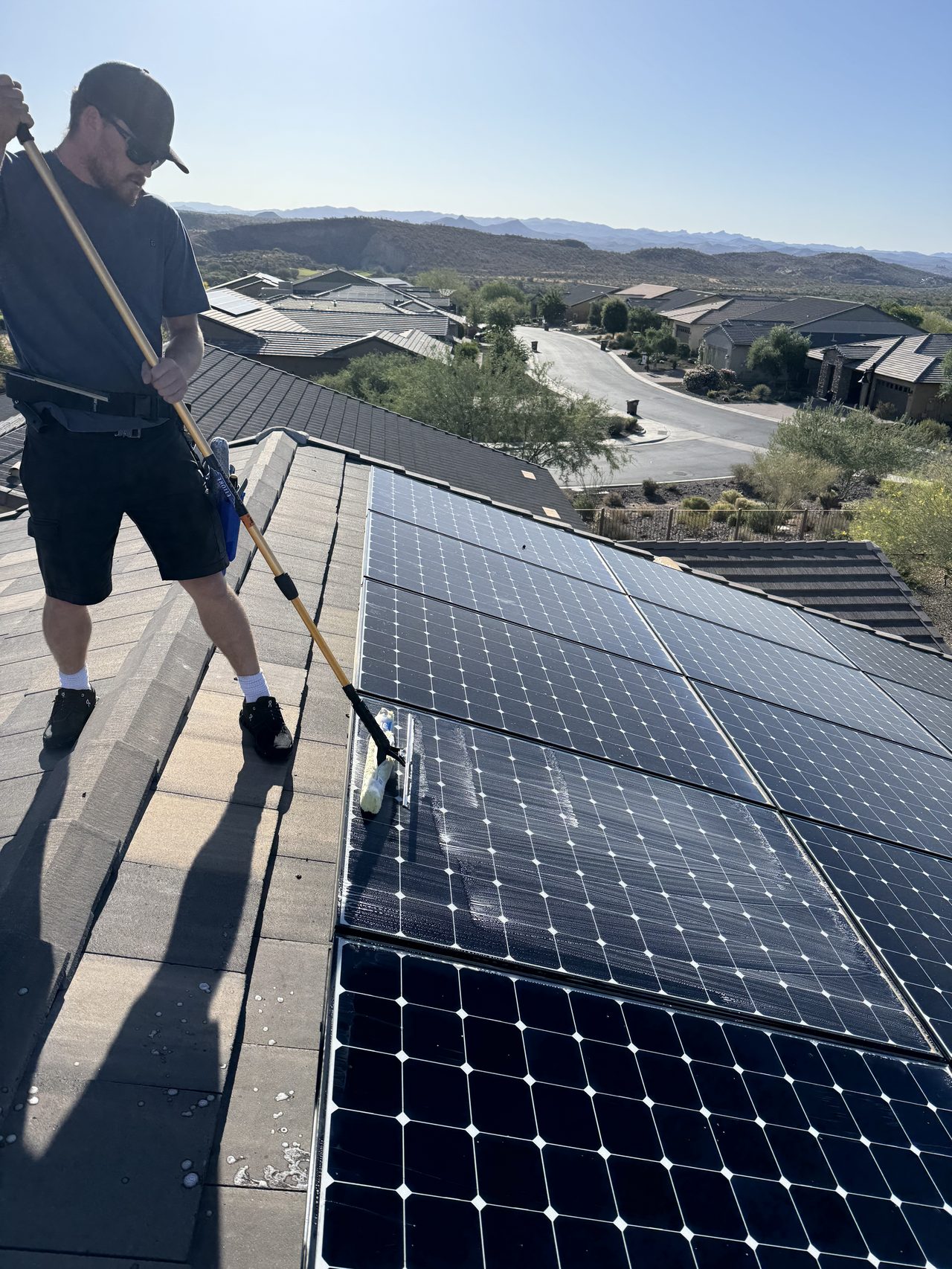 Wicked Shine technician cleaning solar panels on a rooftop with desert mountains behind